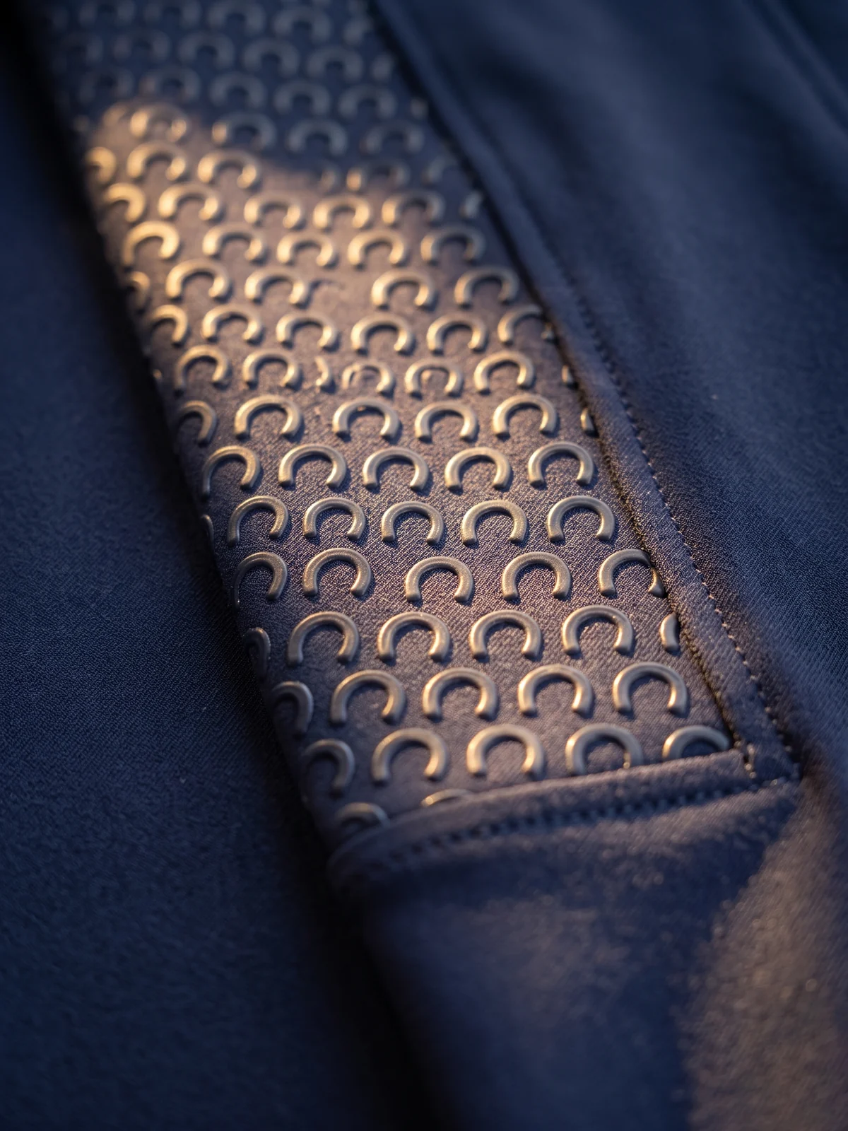 Silikon-Grip mit einem eigenen Logo-Zeichen als wiederholtes Motiv auf dem Knie einer Reithose – KI-generierte Illustration