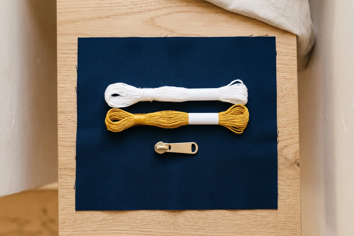 Stoffmuster in Navy mit Stickgarn und einem Zipper-Puller aus Metall – KI-generierte Illustration