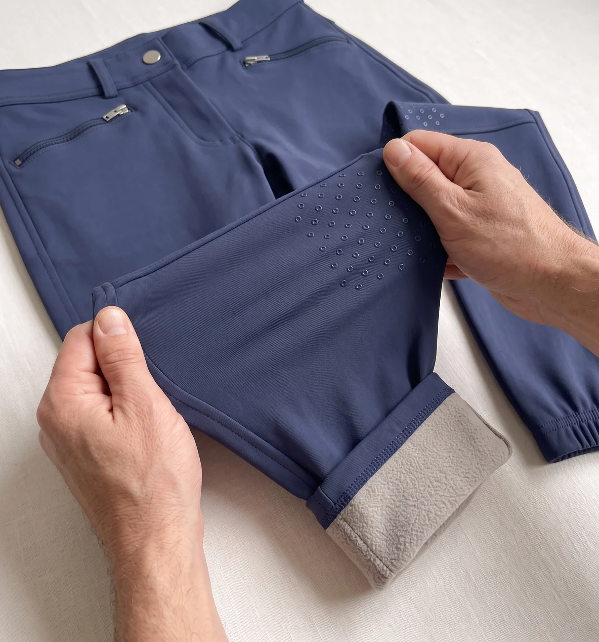 Zwei Hände dehnen den Stoff an der Grip-Fläche einer Navy Winterreithose, das Fleecefutter blitzt am Rand – KI-generierte Illustration